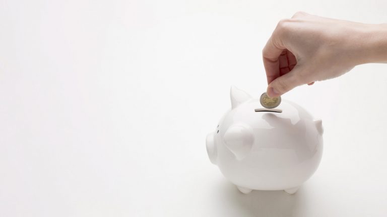 Coin being inserted into a white piggy bank