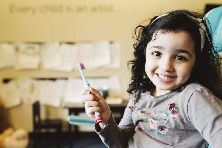 portrait of a child holding a toothbrush while smiling at the camera