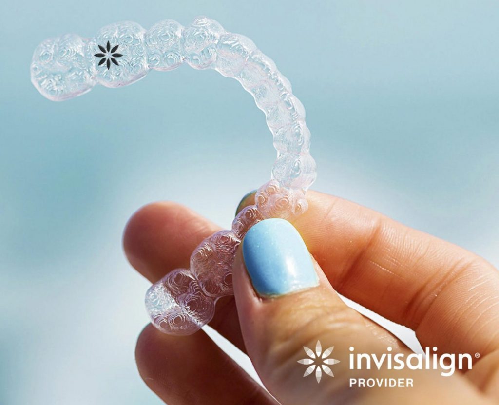 a hand holding an invisalign clear aligner in front of a blue background