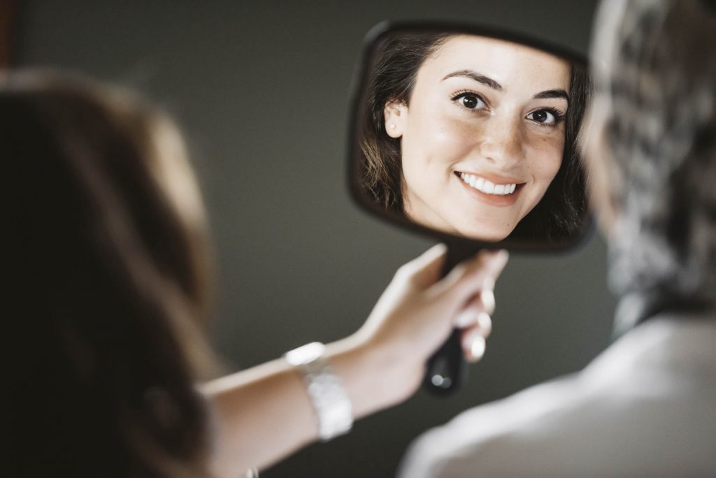 a woman holding a mirror and looking at herself and smiling