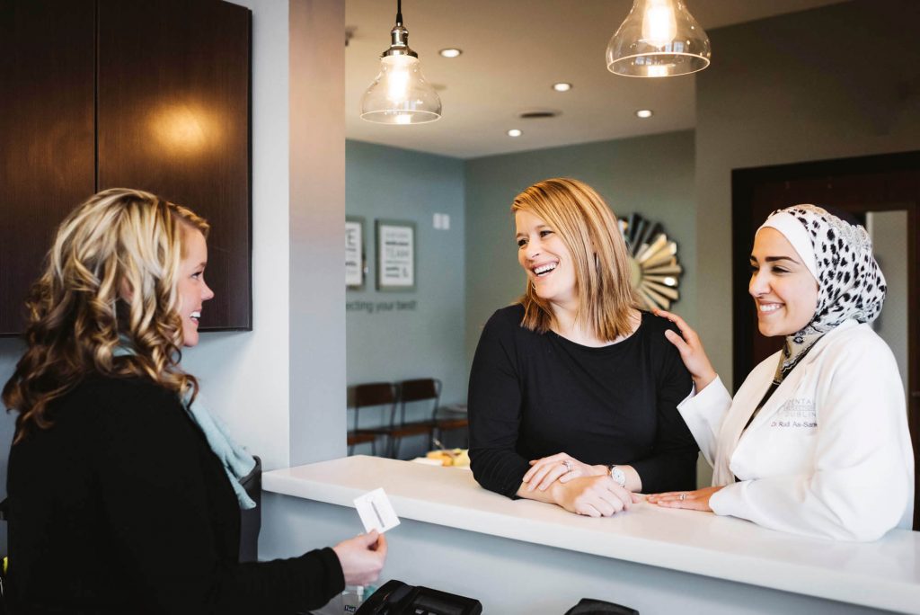 dentist and patient stand at the front desk in a dental office and talk to the receptionist