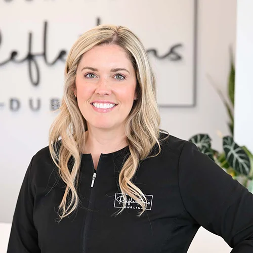 Headshot of Allison wearing a black jacket with 'Dental Reflections Dublin' logo, standing against a blurred background featuring the same logo.