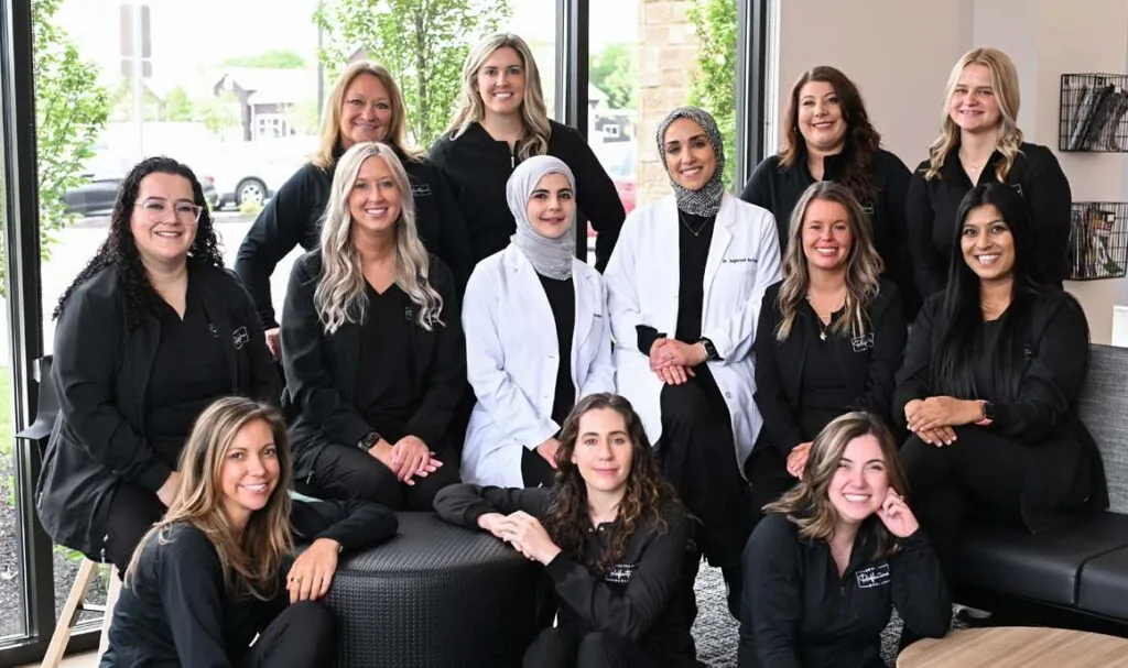 Group photo of 13 individuals dressed in black, except two wearing white lab coats, posed in a professional indoor environment with a mix of seated and standing positions.