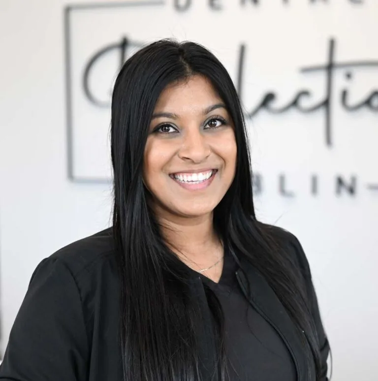 Headshot of Prathana wearing a black jacket with 'Dental Reflections Dublin' logo, standing against a blurred background featuring the same logo.