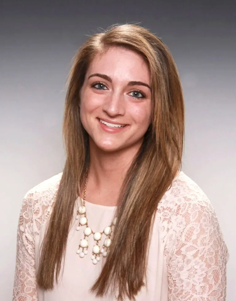 Headshot OF Dr. Bartlett wearing a top with lace in sleeves and a necklace. The background is color gray.